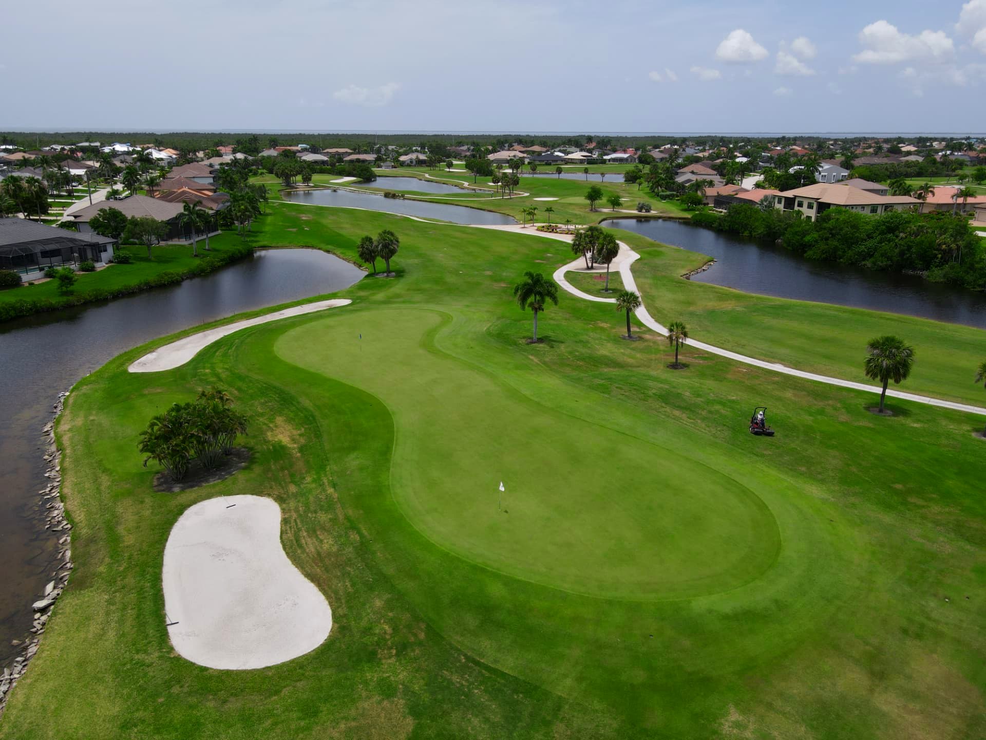 Aerial view of a lakeside green framed by palms and a large bunker
